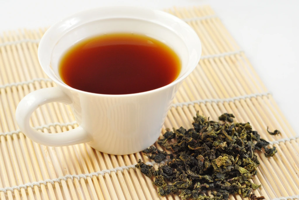 Black Tea on a white glass cup beside on black tea plant placed on a wooden table