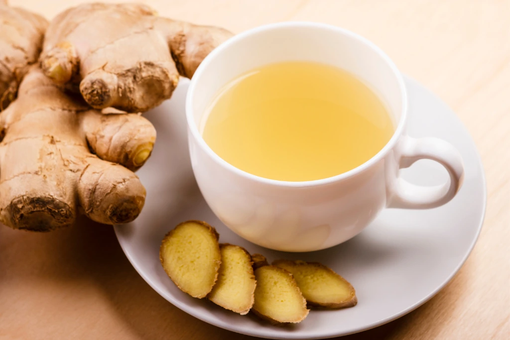 A cup of Ginger Tea on a white glass cup with ginger slices on its side