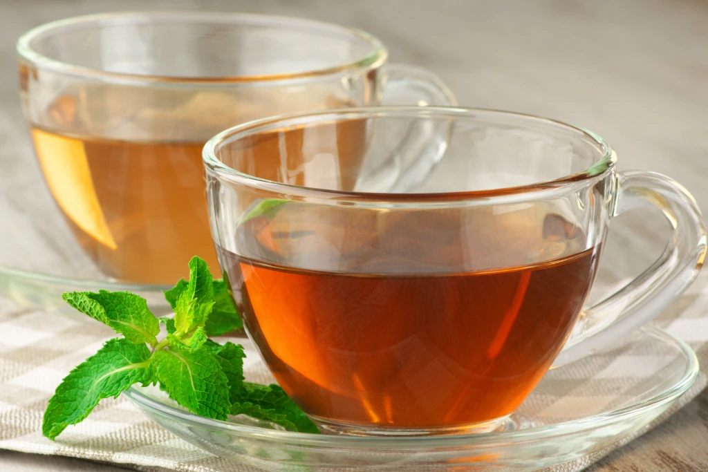 green tea on top of a saucer with green tea leaves by its side