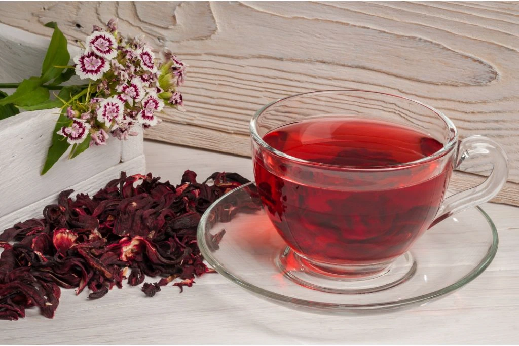 hibiscus tea on top of a saucer with dried hibiscus petals by its side