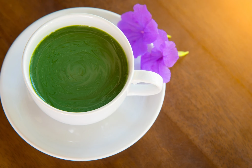a cup of matcha tea with fresh flowers on a wood table