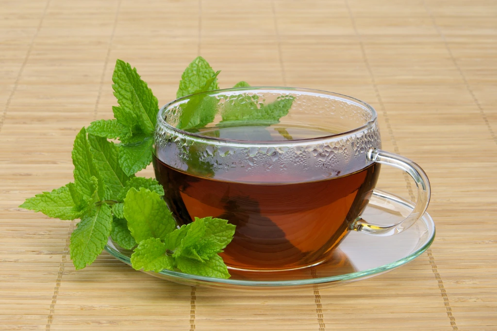 Peppermint Tea on a glass cup on a brown table with a peppermint tea leaves