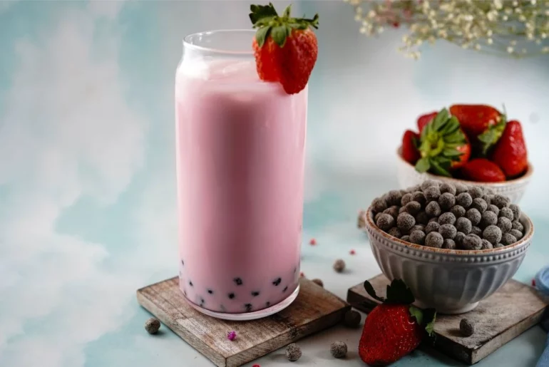 Strawberry milk tea is in a glass jar with a bowl beside it filled with pearls.
