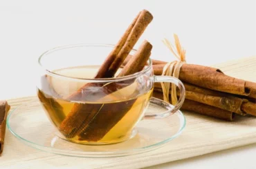 Glass cup filled with cinnamon tea surrounded by cinnamon on a white background