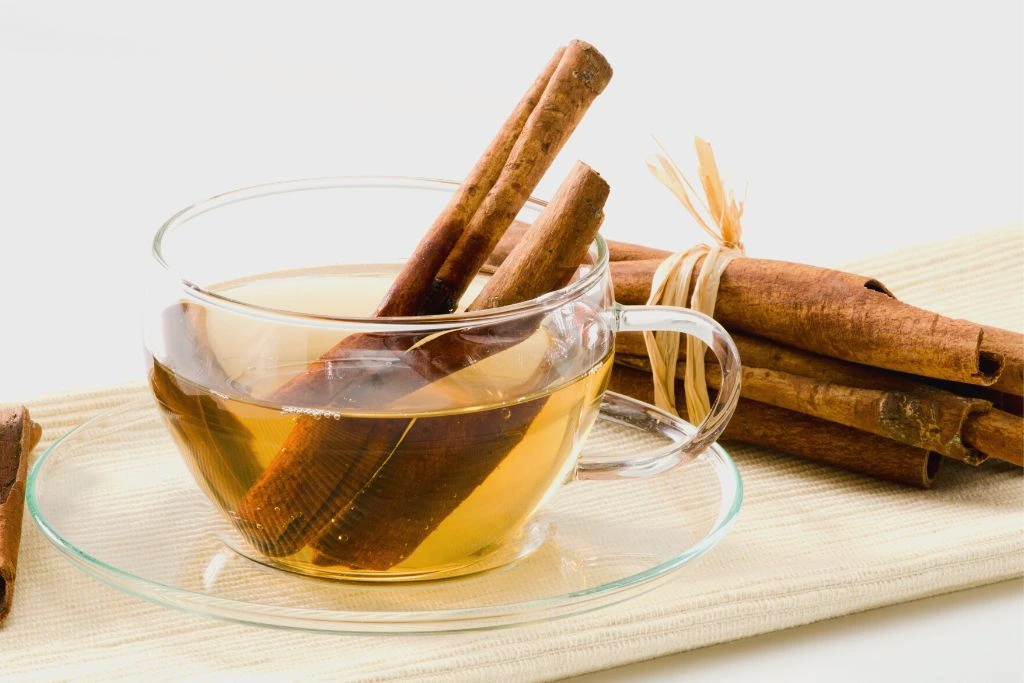 Glass cup filled with cinnamon tea surrounded by cinnamon on a white background