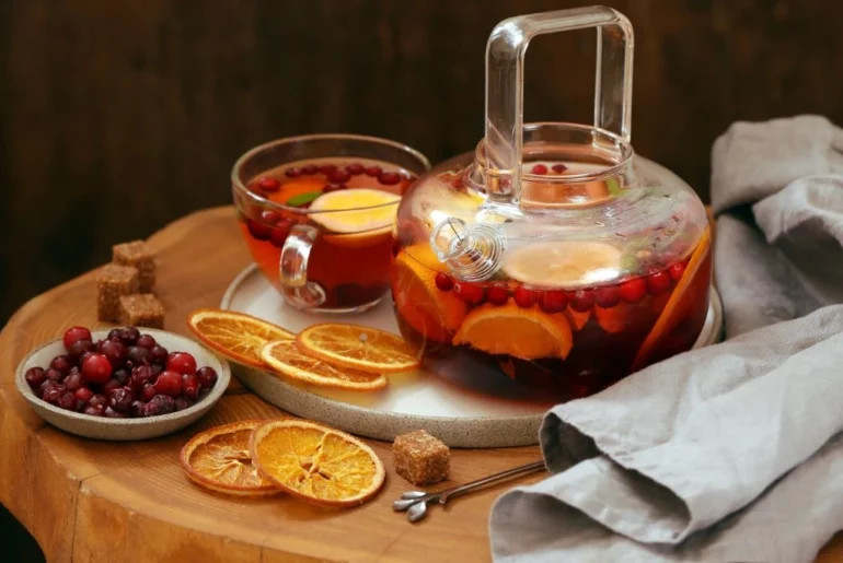 a pot and a cup of cranberry tea with orange slices on a wood board