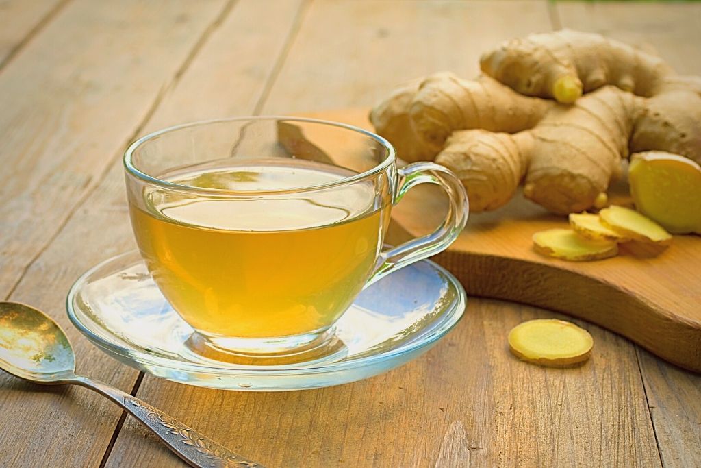 Glass cup filled with ginger tea surrounded by ginger vegetable