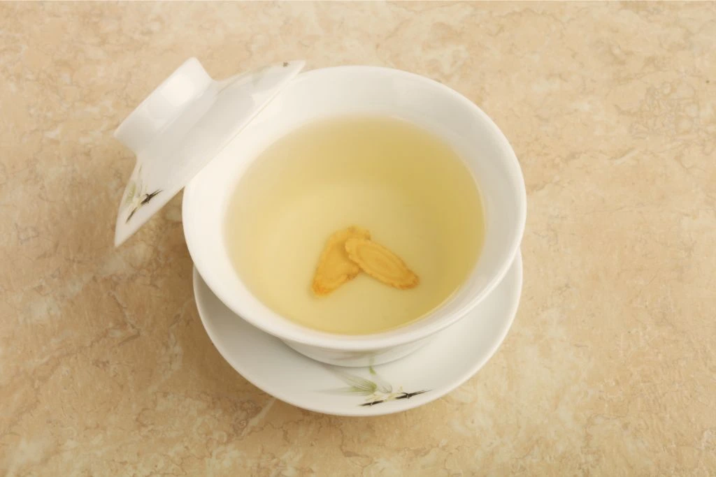 a cup of ginseng tea with ginseng slices in a white ceramic tea cup
