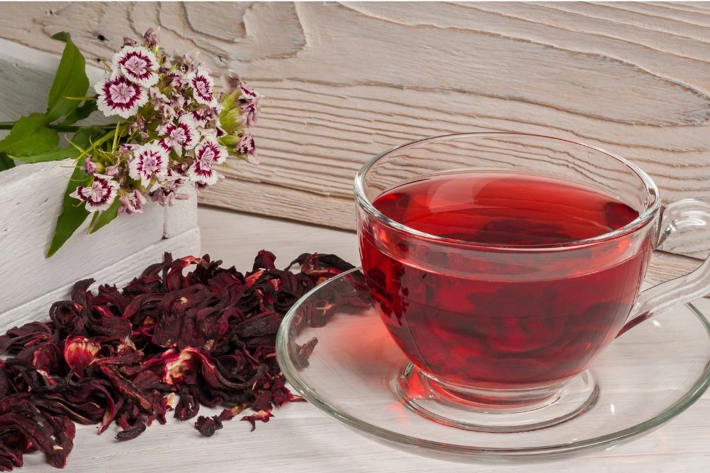 Glass cup filled with hibiscus tea surrounded by hibiscus leaves