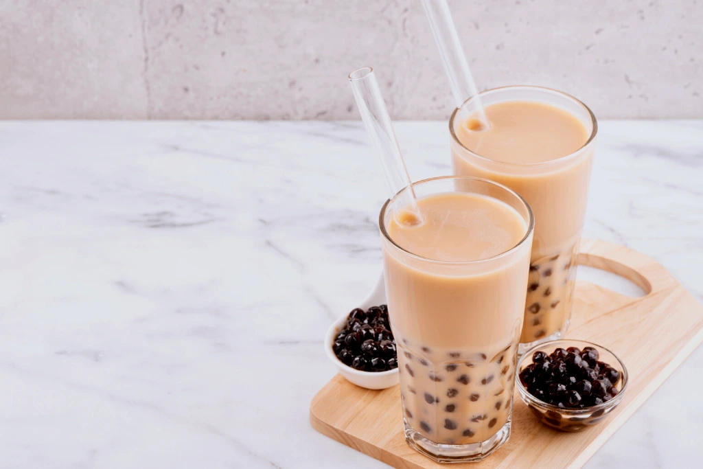 Homemade Milk in a drinking glass with a straw on a marble white table and wooden tray