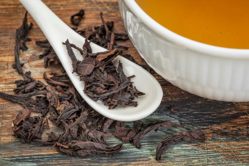 a spoon of dried oolong leaves beside a cup of tea