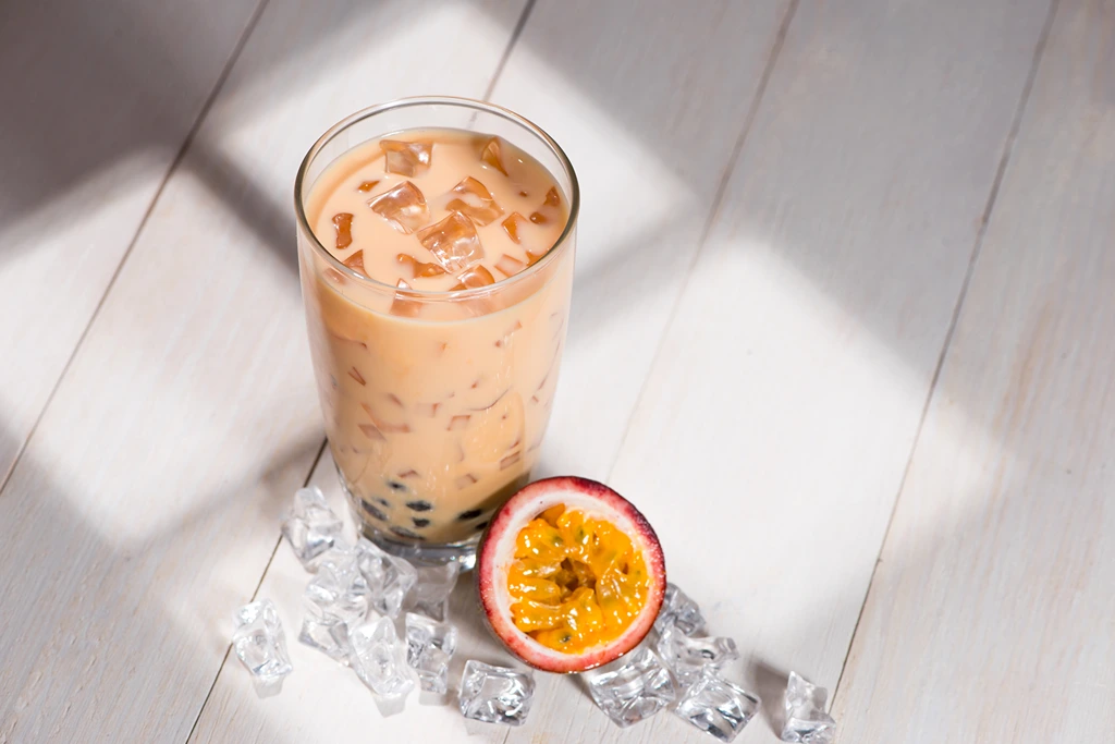 Passion Fruit Boba Milk Tea beside a Passion Fruit with ice cubes around it
