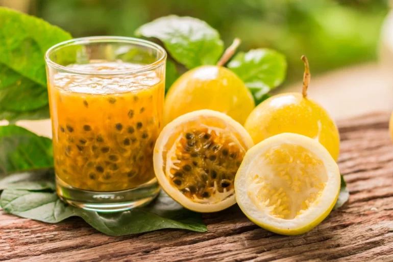 A cup full of Passion Fruit extract with two actual passion fruit on a green-leafy blurry background