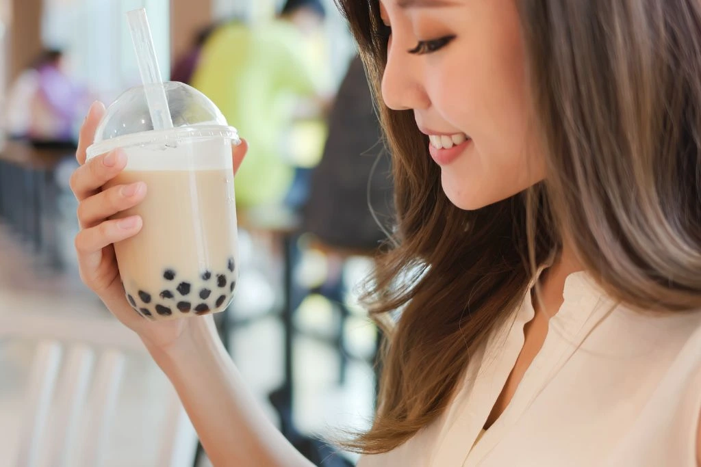 A smiling woman holding a plastic jar of milk tea