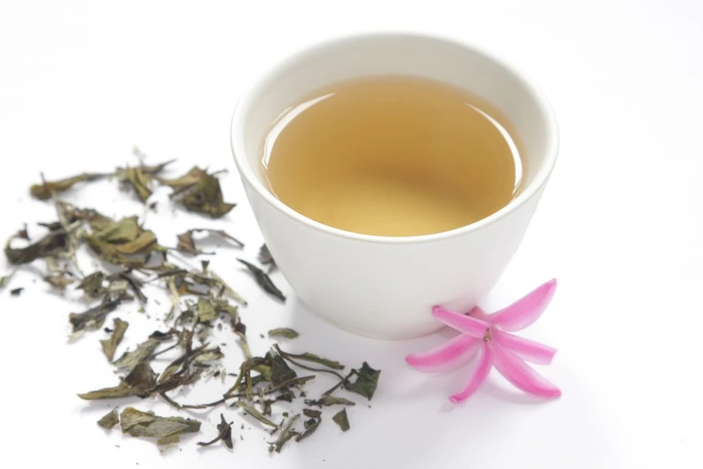 a cup of white tea with dried leaves and a flower on a white background