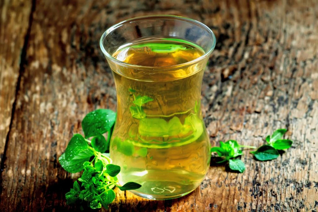 Oregano Tea in a shaped glass jar surrounded by oregano leaves