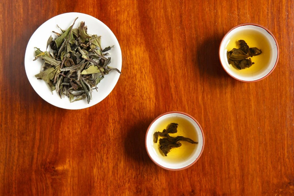 dried tea leaves on a saucer with two cups of tea