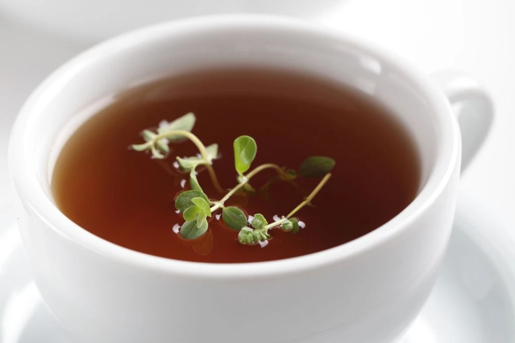 A cup of marjoram tea with marjoram leaves on top of the tea