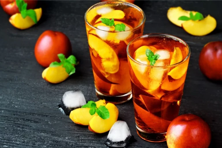 two glasses of full of peach tea surrounded by slices of peach fruit