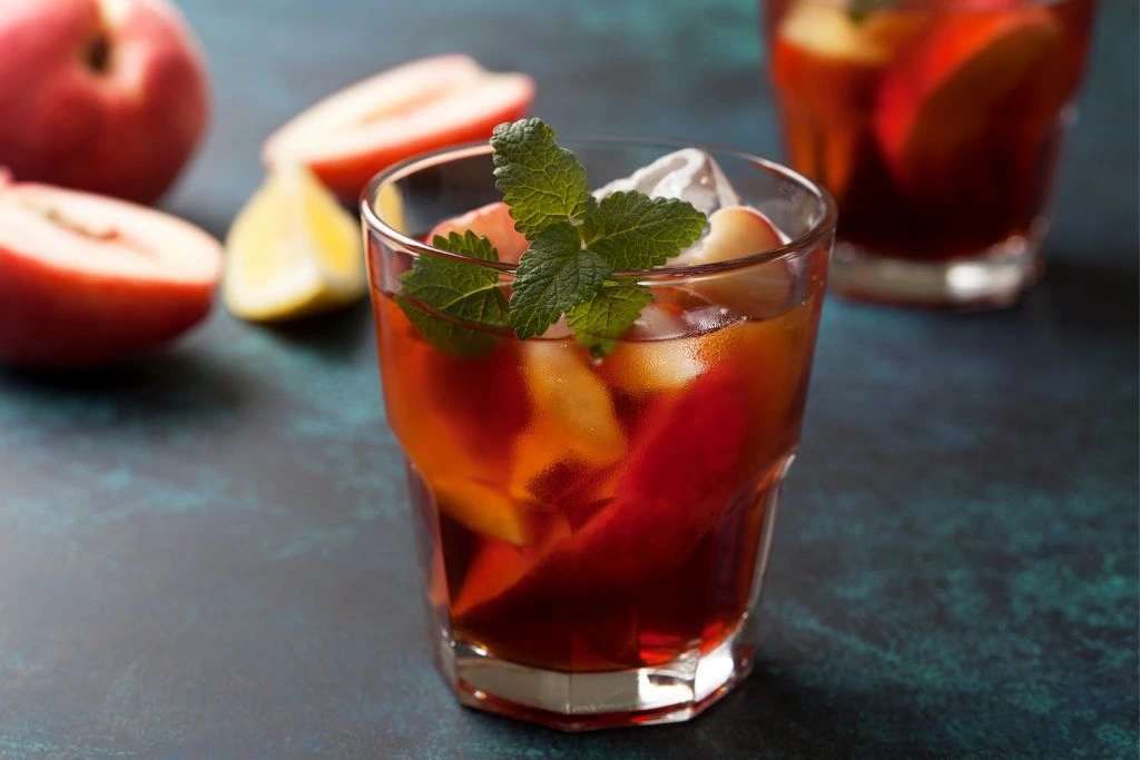 A glass cup is full of slices of peaches and peach tea.