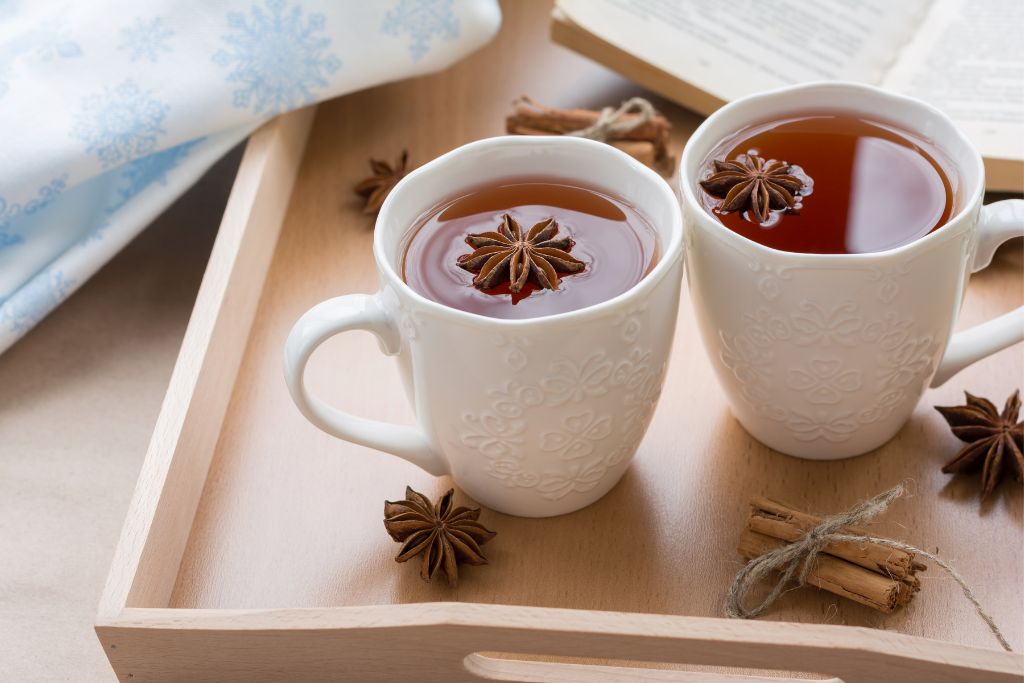 Two cups of star anise tea are prepared and surrounded by anise plants