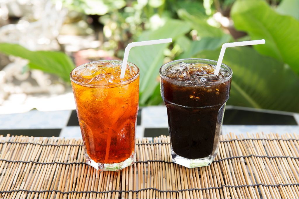 a glass of black iced tea with straws