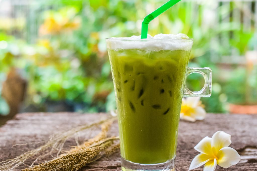 a glass of green iced tea on a wooden table