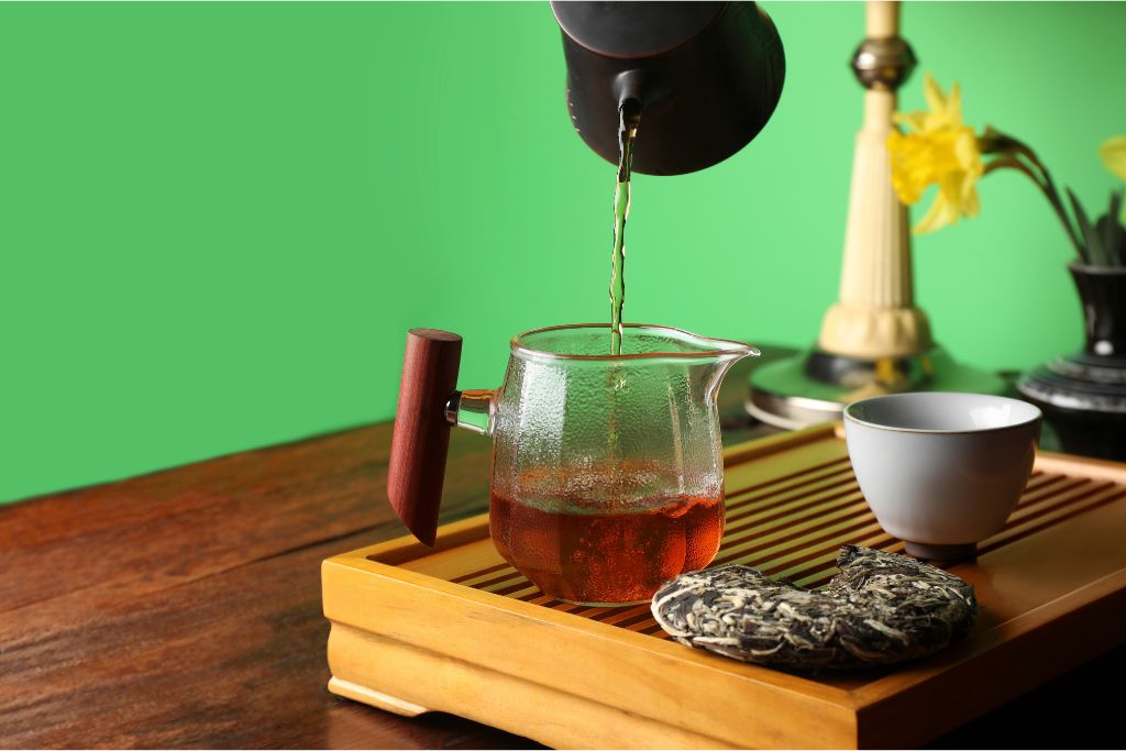 pouring pu erh tea in a glass cup placed in a wooden tray