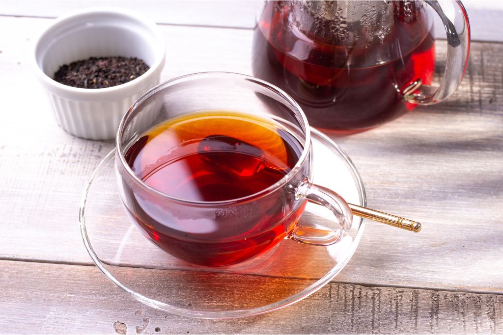 Black tea in a transparent cup with pitcher at the background