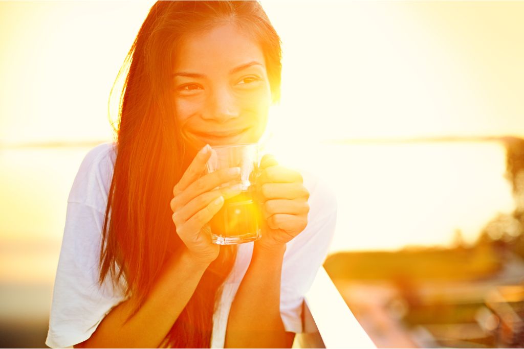 Happy girl is drinking a cup of tea during sunset