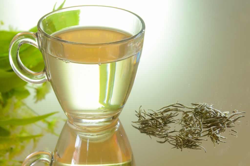 A cup of white tea with tea leaves on the side