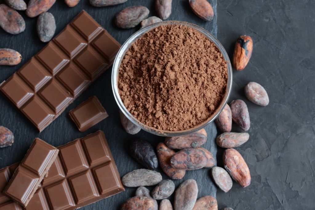 cacao powder on a small cup together with chocolate bars and cocoa beans beside it