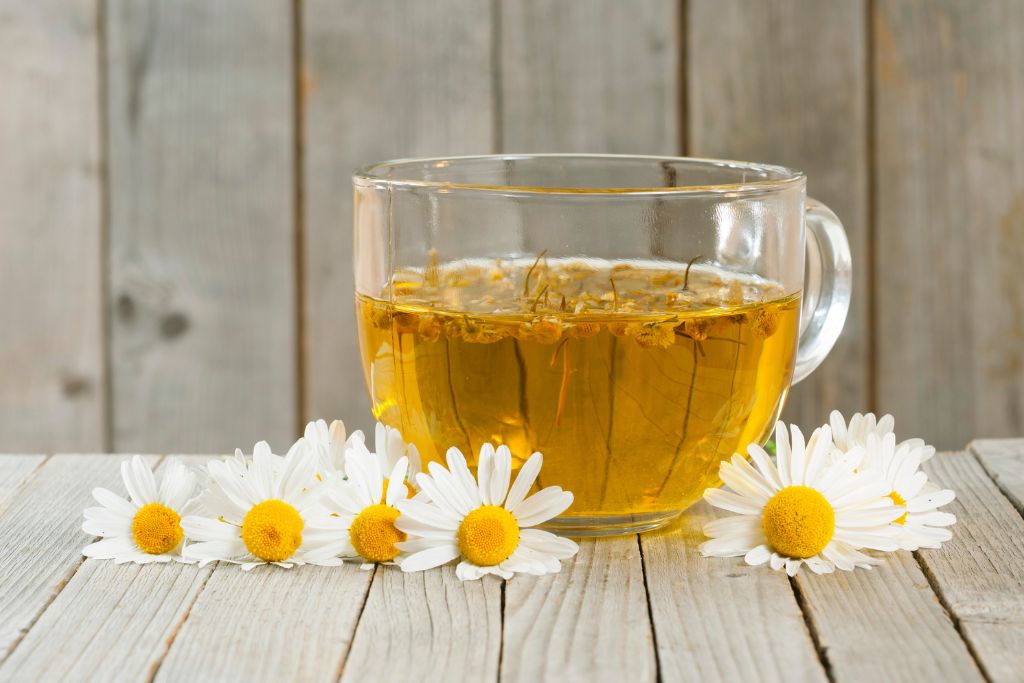 transparent tea cup with chamomile flower beside it situated on a table