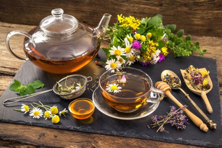 a cup of tea with herbal leaves or flowers, honey, and tea infuser