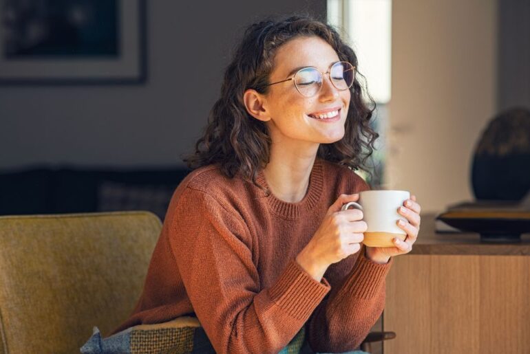 a woman wearing brown long sleeves while holding a white cup