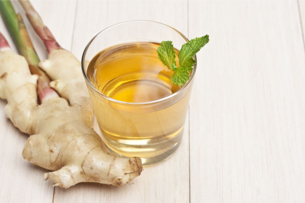 a glass of ginger tea beside a ginger on a white background
