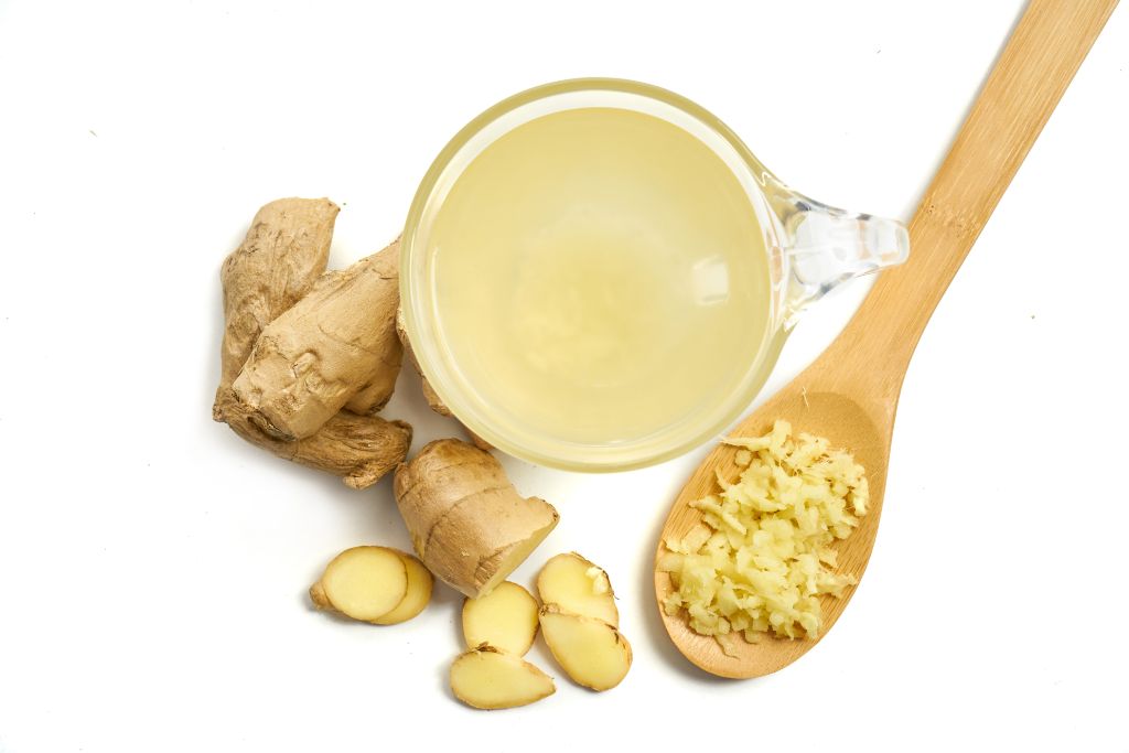 cup of ginger tea with sliced and grated ginger on a wooden spoon