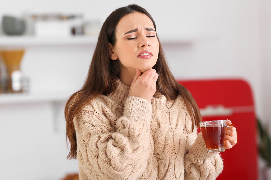 a woman in the kitchen suffering from sore throat while holding a cup of tea for ease