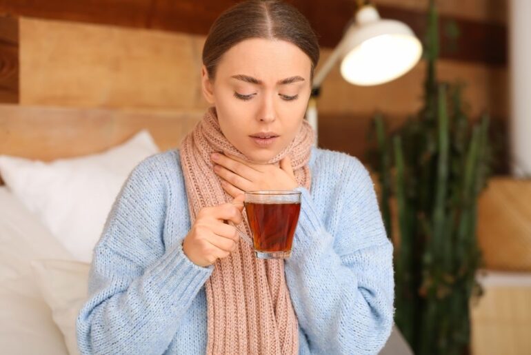 a woman with sore throat drinking hot tea at home