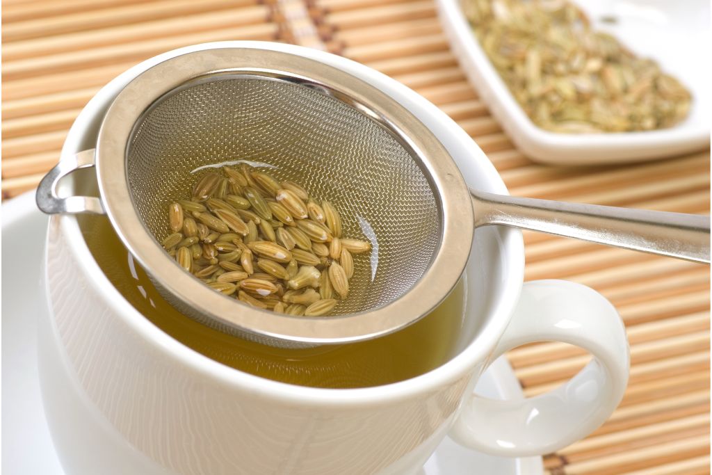 a white cup with dried fennel seed on a strainer soaked in water