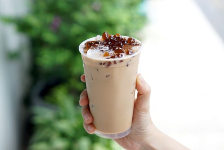 a hand holding a cup of Assam Milk Tea on an outdoor setup