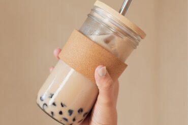 a hand holding a glass of Chai Bubble Tea with pearls on a cream background
