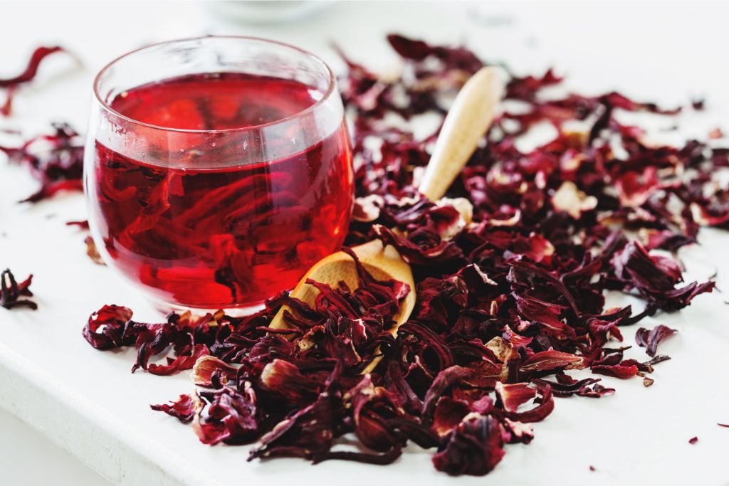  glass of Hibiscus tea surrounded by dried hibiscus petals