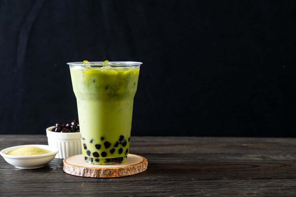 pandan milk tea on a plastic cup with sugar and tapioca pearls in separate bowls