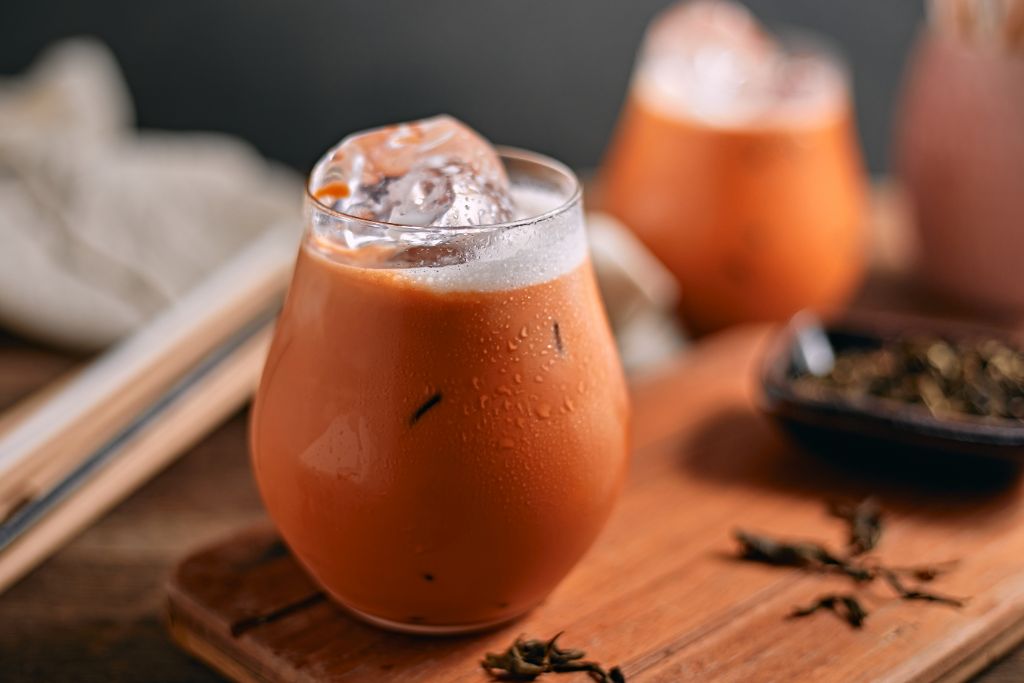 a glass of cold Thai Iced Tea placed on a wood board