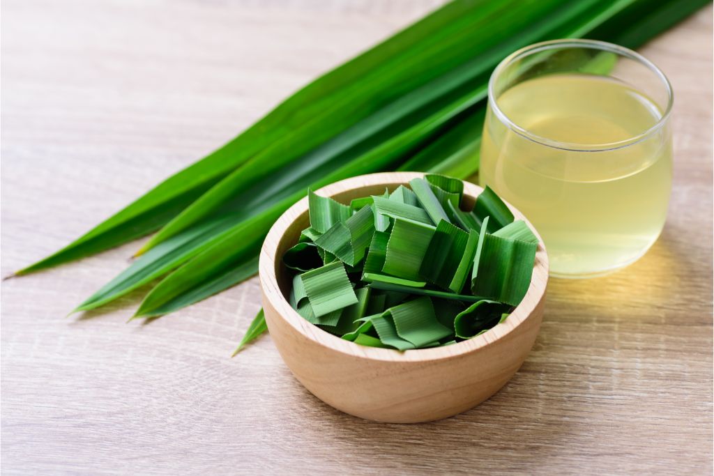 small pieces pandan leaves in a bowl with a glass of pandan drink beside it